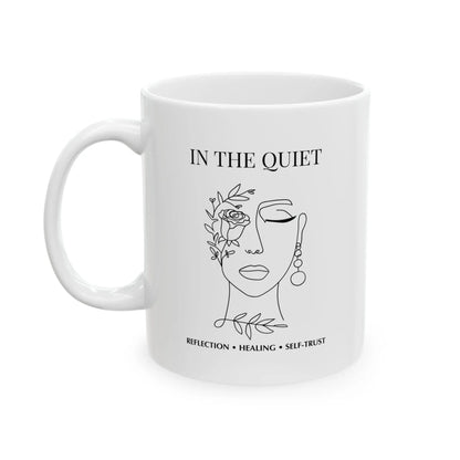 White ceramic mug featuring “In The Quiet” text and minimalist floral face illustration on a clean white background.