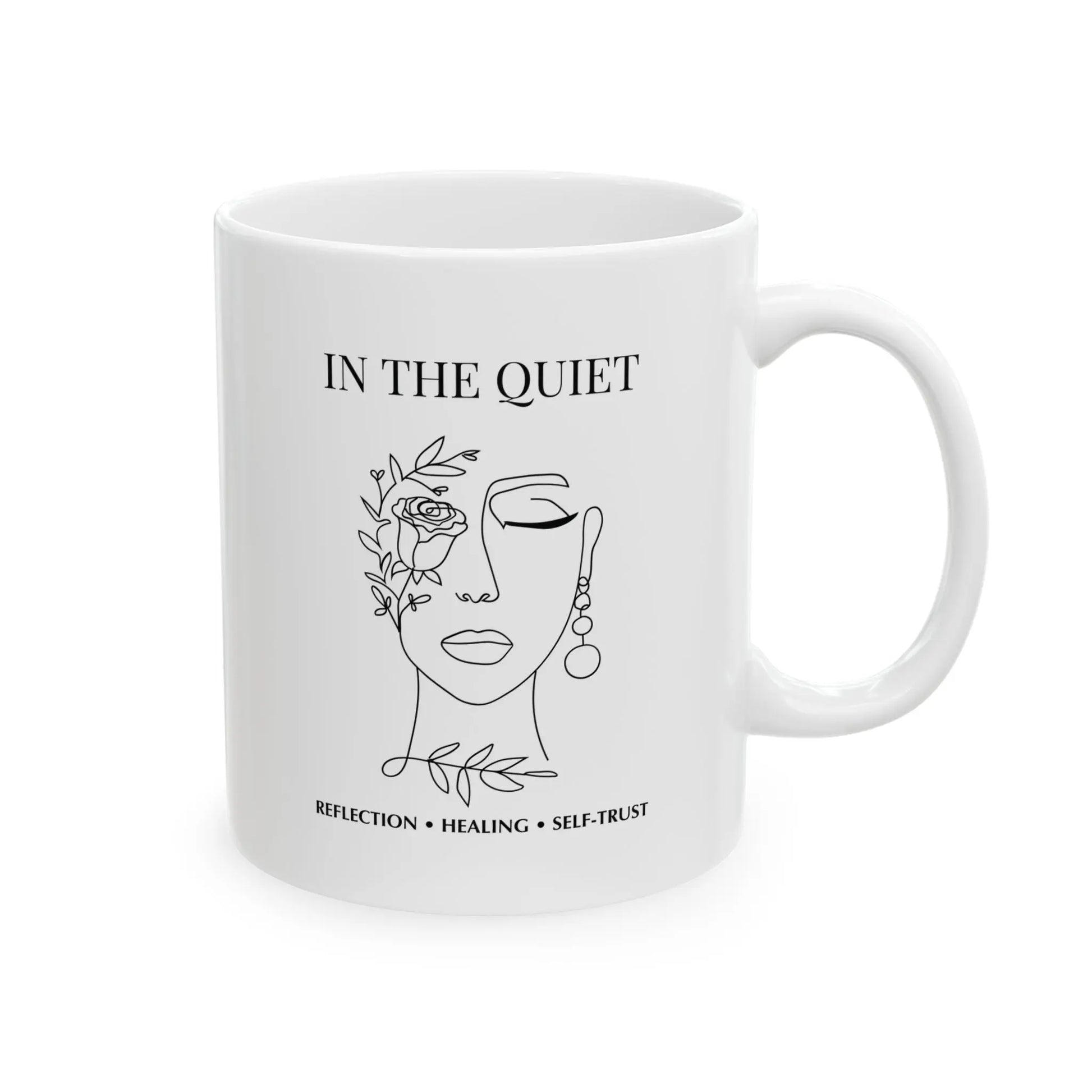 White ceramic mug featuring “In The Quiet” text and minimalist floral face illustration on a clean white background.