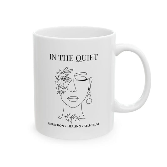 White ceramic mug featuring “In The Quiet” text and minimalist floral face illustration on a clean white background.
